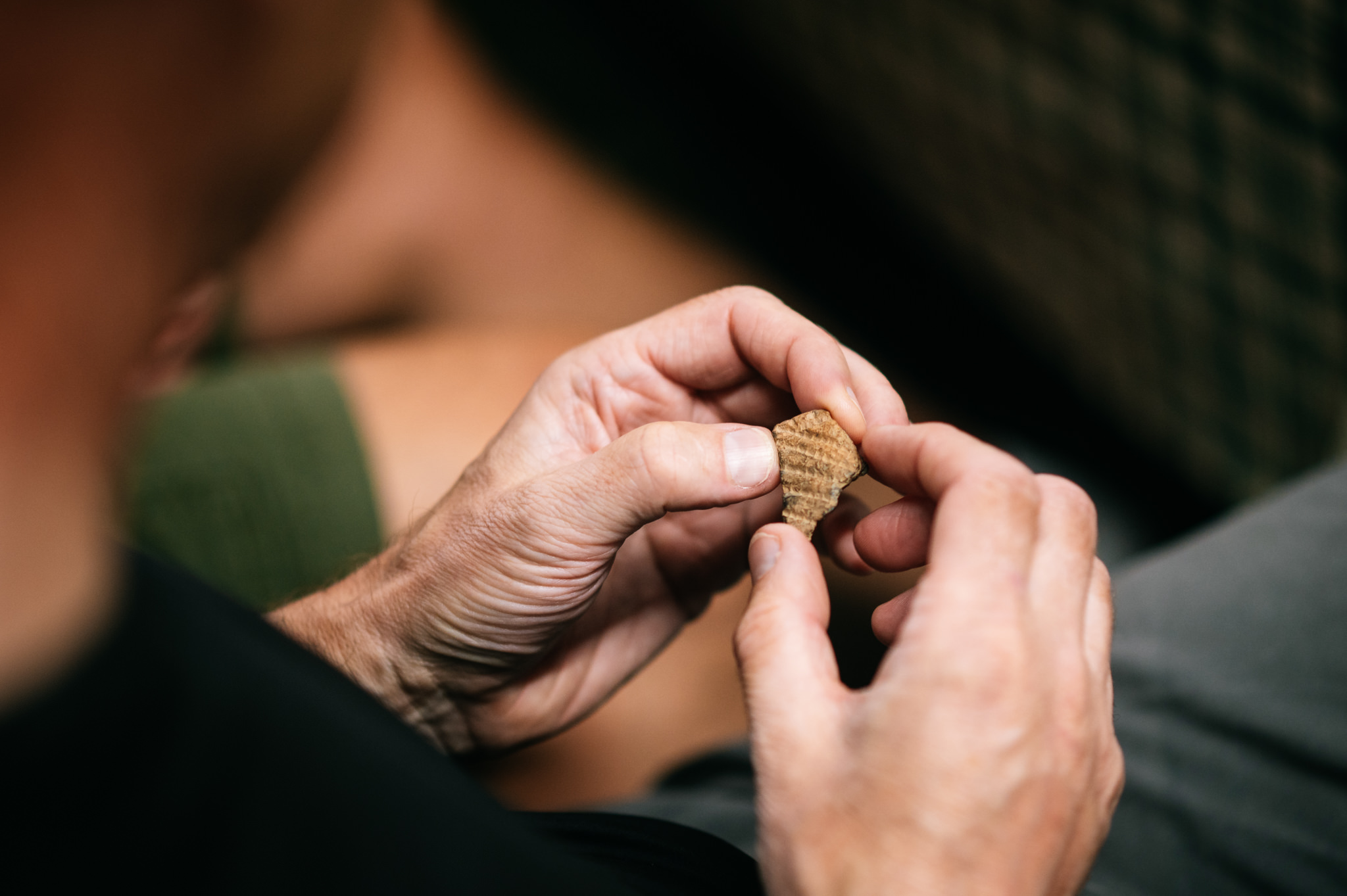 close up of hands examining a small pot sherd