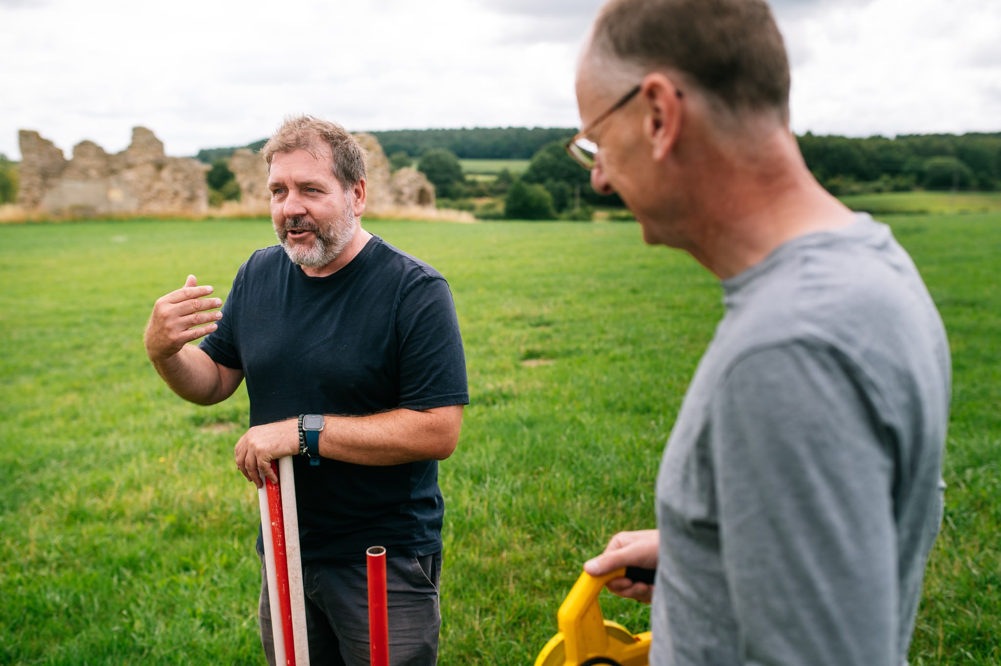 archaeologist holding ranging poles talking to a student
