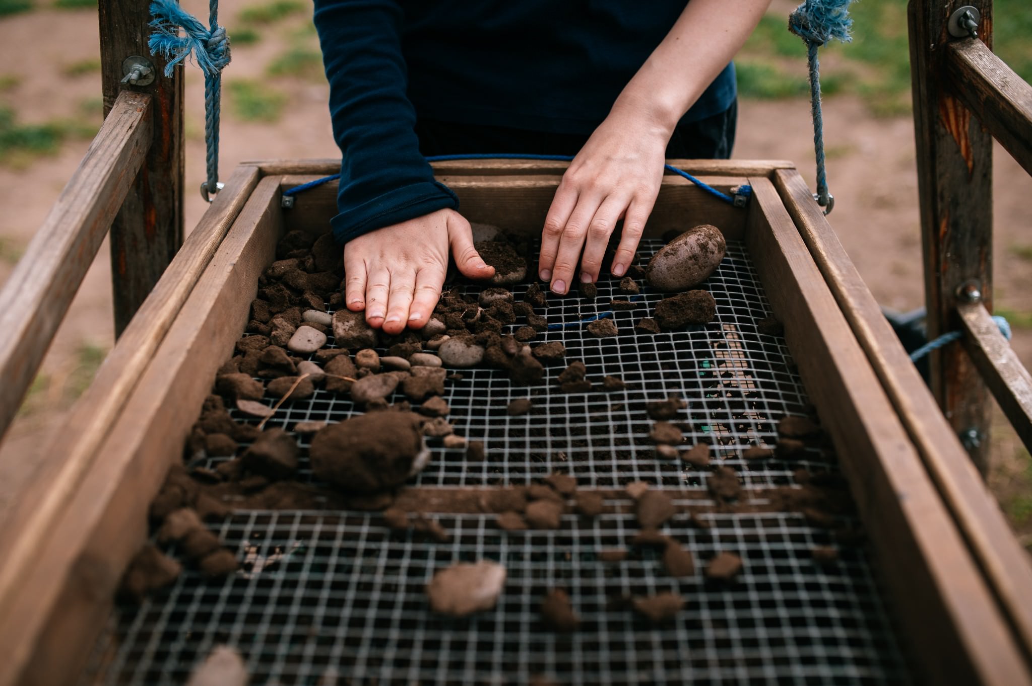 a person's hands using a sieving tray to sort through the trench spoil