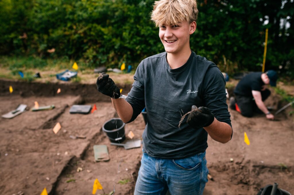 smiling archaeology student wearing black gloves and holding up some finds