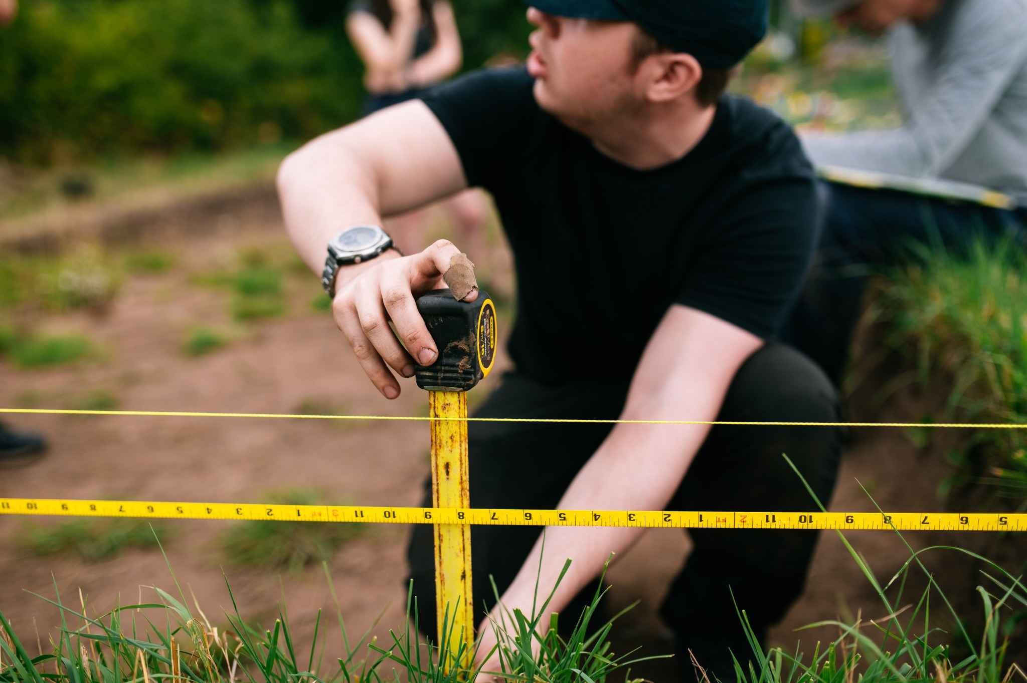 man holding a tape measure against the section of a trench