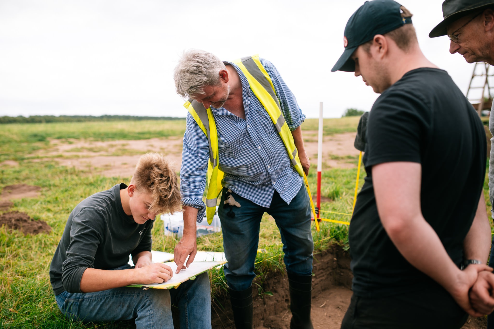 an archaeologist wearing a yellow high-vis vest teaching students about archaeological section drawing