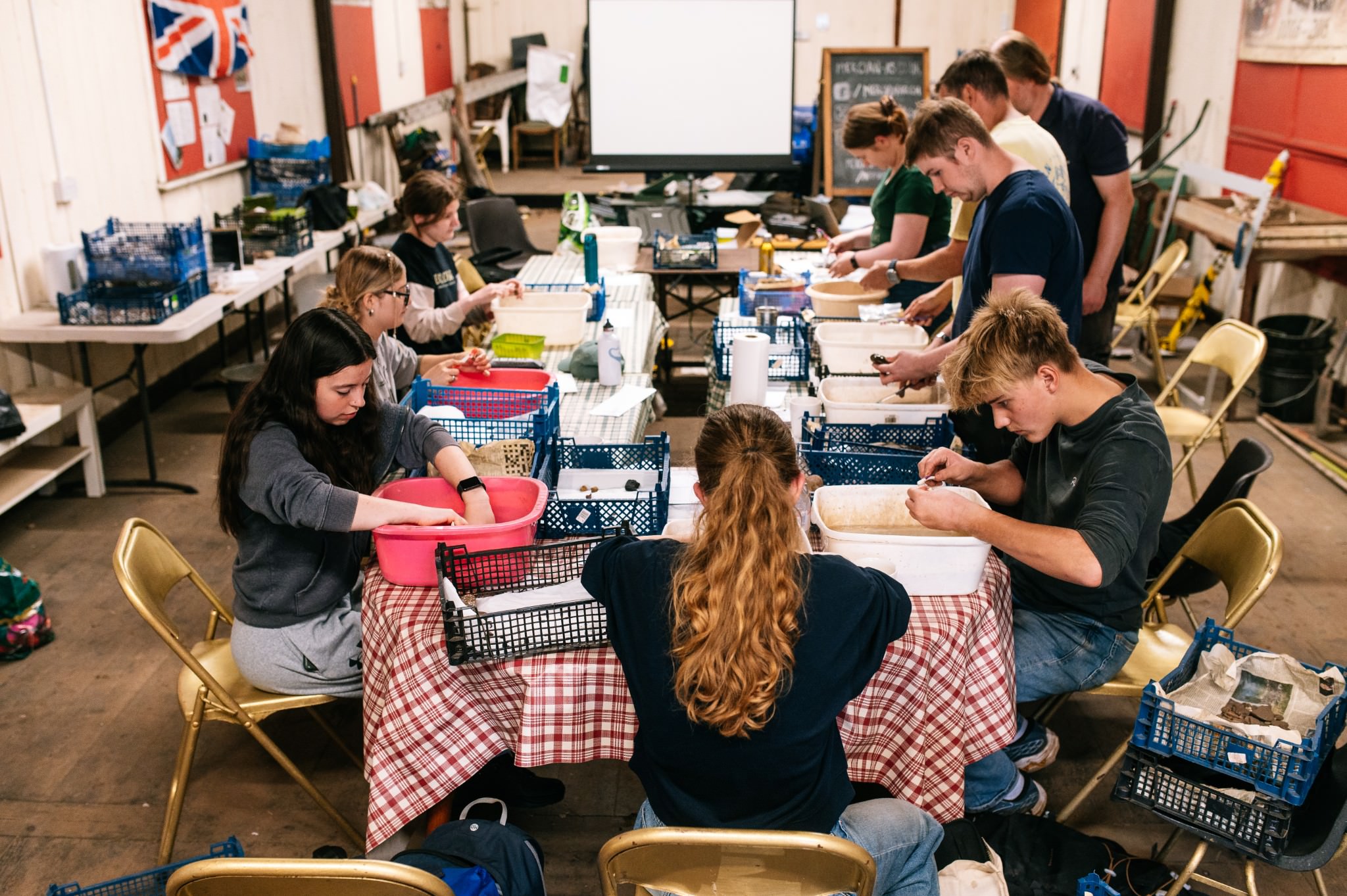 a classroom full of delegates cleaning archaeological artefacts in washing up bowls.