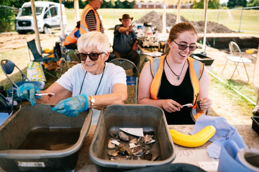 happy archaeology volunteers cleaning finds in washing up bowls